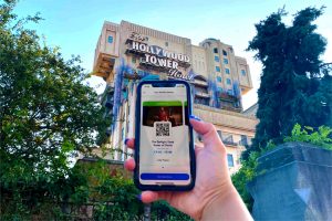 A mobile phone in front of Tower of Terror showing the new Standby Pass screen in the Disneyland Paris app